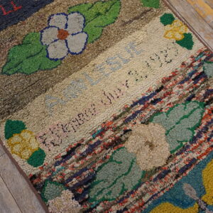 Textured rug with colorful floral motifs, script, and thick multicolored fabric strips on distressed wood floor.
