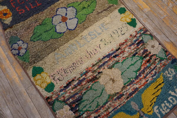 Textured rug with colorful floral motifs, script, and thick multicolored fabric strips on distressed wood floor.