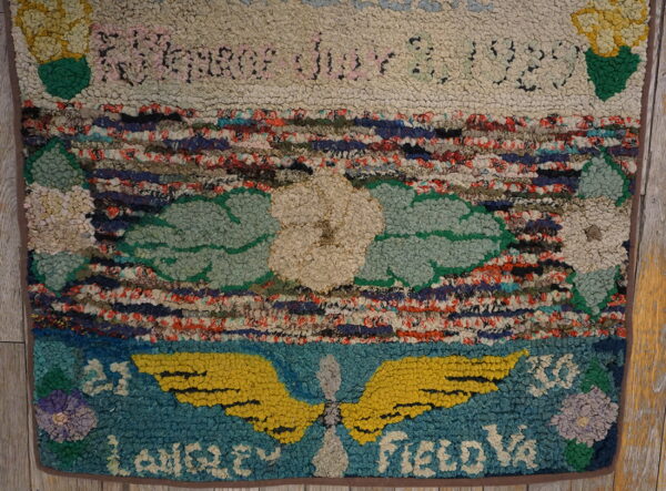 Textured area rug displaying multicolored stripes, floral motifs, lettering, and a yellow winged propeller on wood flooring.