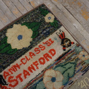 Coarse texture rug with multicolored floral and text patterns lying on weathered gray wood flooring.
