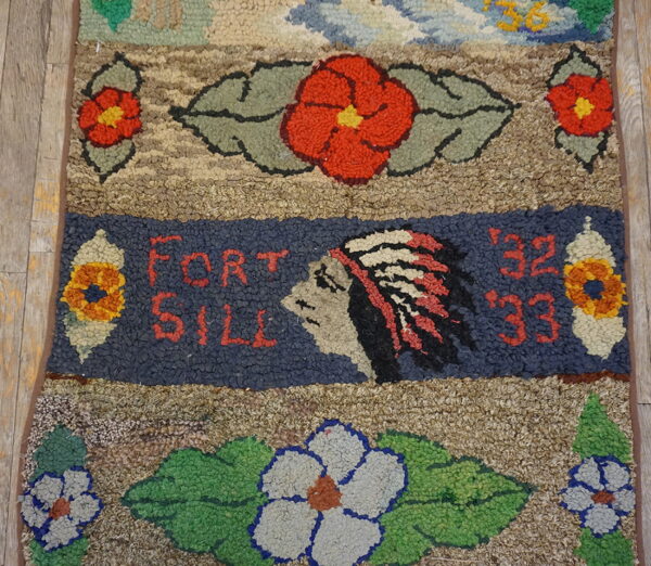 Close-up of a chunky hooked rug featuring red flowers and a dark blue band with "fort sill" text.