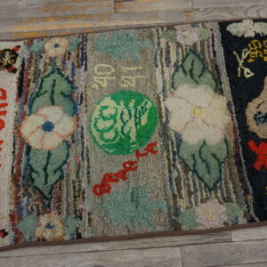 A colorful, high-pile hooked rug featuring striped panels with flowers and stitched lettering lies on wood planks.