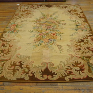 Ornate yellow rug with pastel floral bouquets and a thick brown scrollwork border on distressed wood flooring.