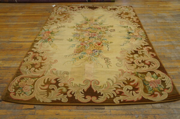 Ornate yellow rug with pastel floral bouquets and a thick brown scrollwork border on distressed wood flooring.