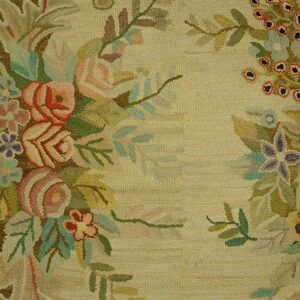 Close-up of a looped rug with multicolored floral garlands on a cream field next to wood flooring.
