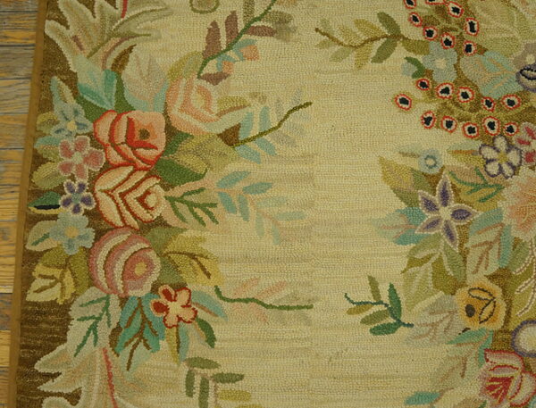 Close-up of a looped rug with multicolored floral garlands on a cream field next to wood flooring.