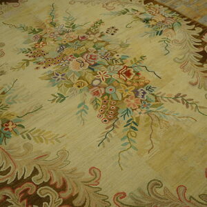 Beige rug featuring a large central bouquet of pastel flowers and a dark brown scrolling acanthus border on wood floor.