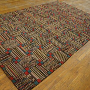 A chunky, multicolored strip rug features a basketweave pattern with intersecting red and teal squares on wood flooring.