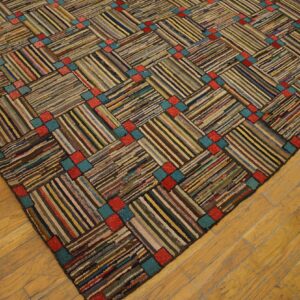 Hooked rag rug with multicolored diagonal stripes, separated by repeating red and teal squares on wood floors.