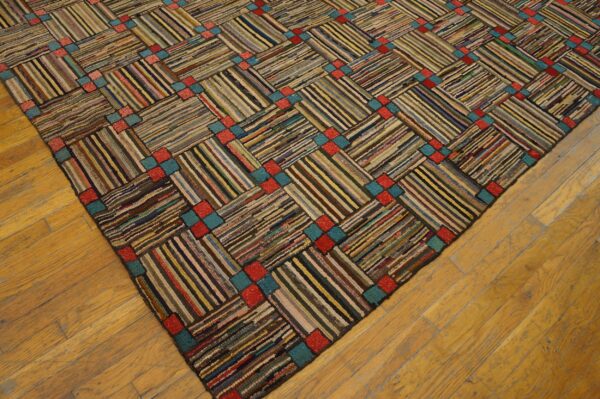 Hooked rag rug with multicolored diagonal stripes, separated by repeating red and teal squares on wood floors.