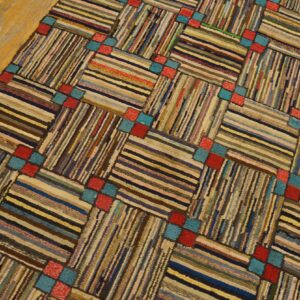 Textured rug with multicolored horizontal and vertical striped blocks linked by red and teal squares on wood flooring.