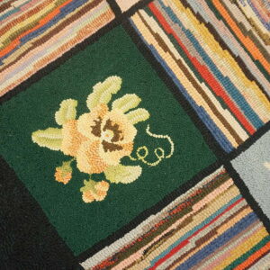 Textured patchwork rug with bold multicolored stripes and a yellow flower motif on a deep green square.