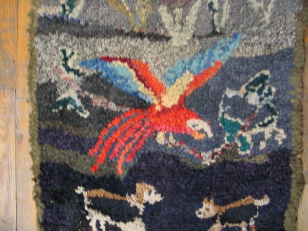 Chunky pile rug with a vibrant parrot design in red, blue, gray, and navy on wood flooring.