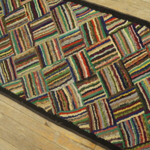 Multicolored striped texture forms a basketweave pattern on a runner rug with a black border on wood planks.