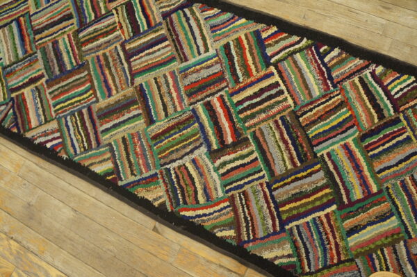 Multicolored striped texture forms a basketweave pattern on a runner rug with a black border on wood planks.