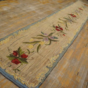 Hooked runner rug with a light background, red floral motif, and blue border, displayed on distressed wood.