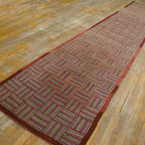 Geometric runner rug with multicolored striped blocks and a red border, lying on worn wood planks.