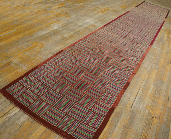 Geometric runner rug with multicolored striped blocks and a red border, lying on worn wood planks.