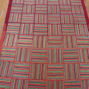 Colorful striped squares alternate directions within a red grid, lying on a wooden plank floor.