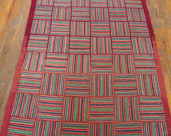 Colorful striped squares alternate directions within a red grid, lying on a wooden plank floor.