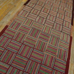 A colorful runner rug with a striped checkerboard pattern rests on worn yellow and gray wood flooring.