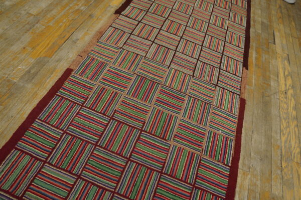 A colorful runner rug with a striped checkerboard pattern rests on worn yellow and gray wood flooring.