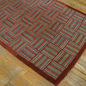 Colorful rug with a checkerboard of red, green, and blue striped blocks and a wide rust border on wood flooring.