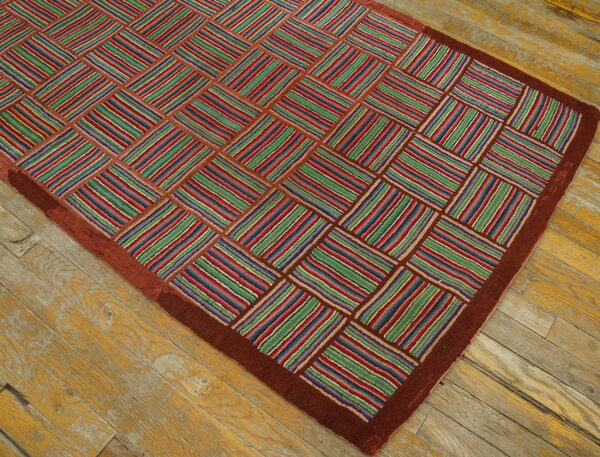 Colorful rug with a checkerboard of red, green, and blue striped blocks and a wide rust border on wood flooring.