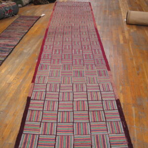 A long runner rug featuring a checkerboard pattern of vertical and horizontal multicolored stripes on wood flooring.