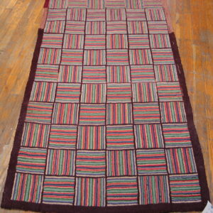 Runner rug with a colorful striped grid pattern and dark border rests on a distressed wood floor.