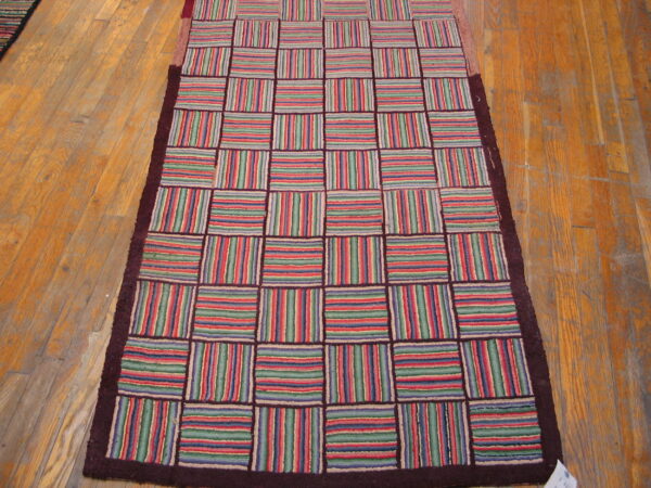 Runner rug with a colorful striped grid pattern and dark border rests on a distressed wood floor.