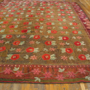 Textured rug featuring red and pink floral motifs on an earth-toned background, laid upon wood plank flooring.