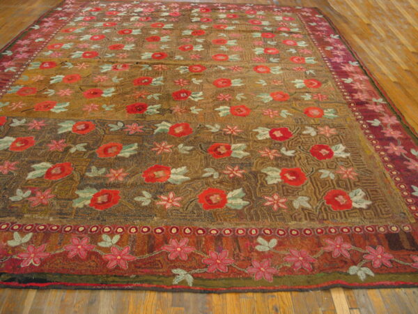 Textured rug featuring red and pink floral motifs on an earth-toned background, laid upon wood plank flooring.