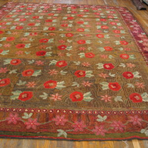 Large, textured pile rug with red floral motifs and burgundy borders on hardwood flooring.