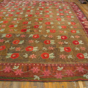 Rustic gold and brown low-pile rug with dense red and pink floral patterns on wood plank flooring.