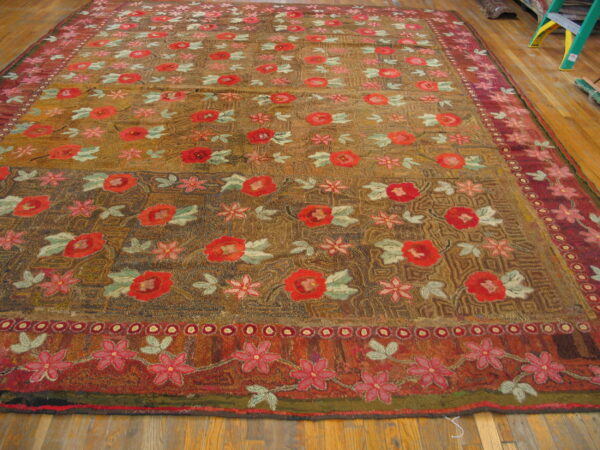 Rustic gold and brown low-pile rug with dense red and pink floral patterns on wood plank flooring.