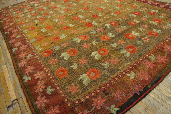 Textural rug in gold, red, and brown colors with a dense floral pattern lies on worn wood flooring.