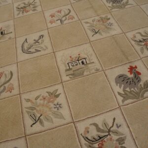 Cream and tan low-pile rug with checkerboard squares showing pictorial motifs like roosters and houses.