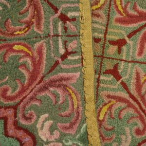 Textured green rug with red and pink scrollwork motifs, separated by a visible vertical burlap seam.