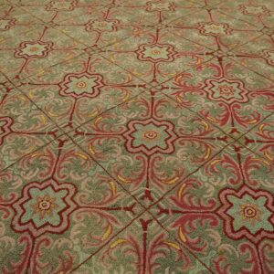 Textured rug displaying a repeating pattern of pink and red ornamental medallions on a muted green ground.