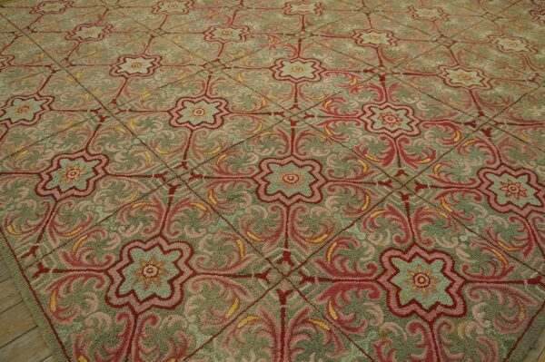 Textured rug displaying a repeating pattern of pink and red ornamental medallions on a muted green ground.