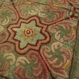 Intricate looped rug detail featuring green, blush pink, and red scrolls over rustic wood planks.