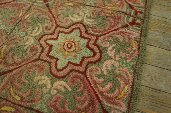 Intricate looped rug detail featuring green, blush pink, and red scrolls over rustic wood planks.
