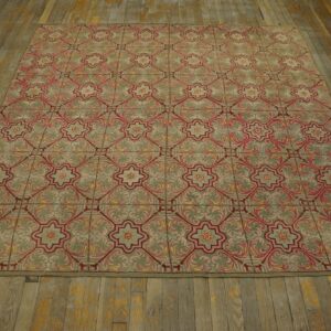 Muted green rug with repeating red and pink floral lattice pattern resting on worn wood flooring.