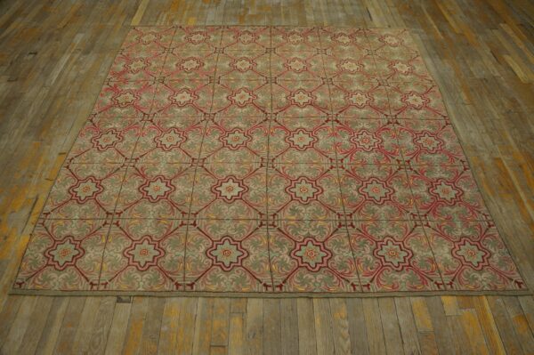 Muted green rug with repeating red and pink floral lattice pattern resting on worn wood flooring.