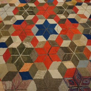 Multicolored high pile rug displaying a geometric tumbling block pattern in red, blue, beige, and olive green.