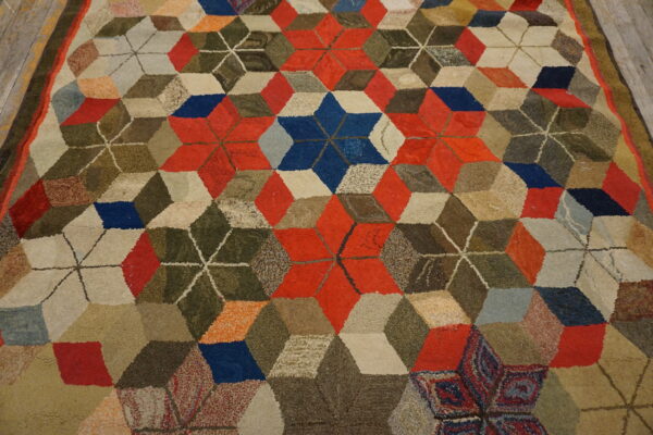 Multicolored high pile rug displaying a geometric tumbling block pattern in red, blue, beige, and olive green.