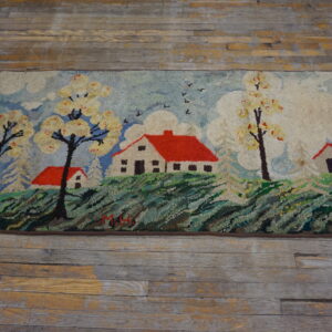 Textured scenic rug featuring white houses with red roofs and flowering trees on worn wood flooring.