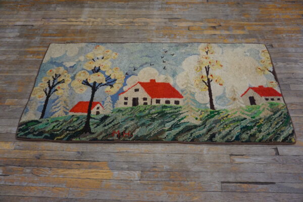Textured scenic rug featuring white houses with red roofs and flowering trees on worn wood flooring.