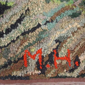 Chunky textured rug in greens, browns, and black with clearly visible red initials M.H.